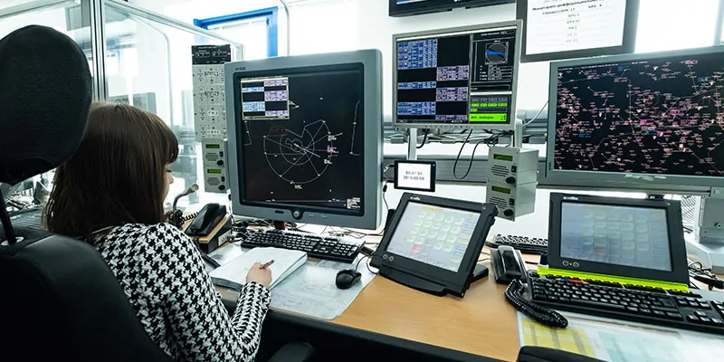 Controladora aérea supervisando tráfico en sala de monitoreo con múltiples pantallas
