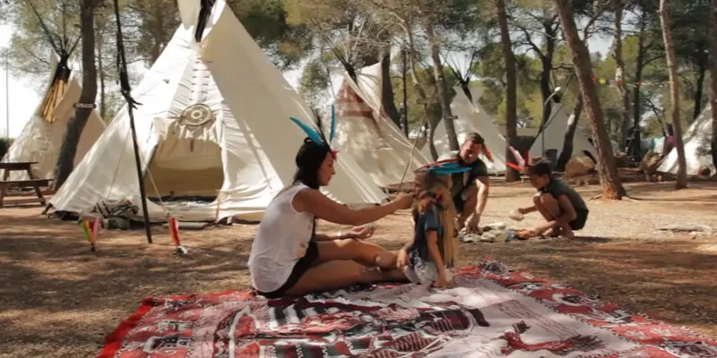 Familia jugando en campamento de tipis rodeado de árboles durante experiencia temática al aire libre