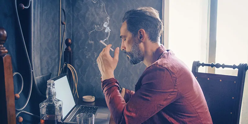 Hombre pensativo trabajando con portátil mientras fuma en ambiente íntimo