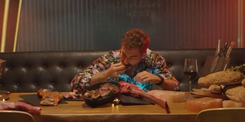 Hombre comiendo un corte de carne en un restaurante con vino tinto