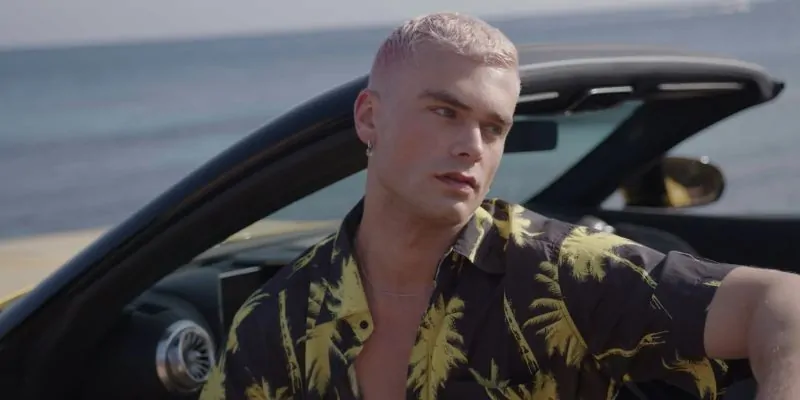 Modelo posando con camisa tropical junto a coche descapotable frente al mar